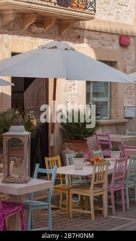 A table with multi-colored chairs under a parasol in front of a house Stock Photo