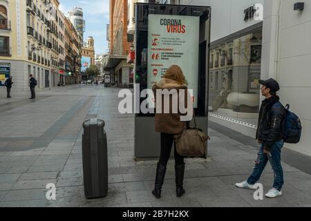Two pedestrians look at an information sign warning about coronavirus in Preciados street, in Madrid's city center, following coronavirus lockdown Stock Photo