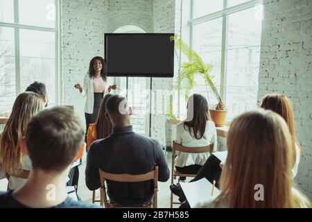 Pointing. Female african-american speaker giving presentation in hall at workshop. Audience or hall. Rear view of participants. Conference event, training. Education, diversity, inclusive concept. Stock Photo