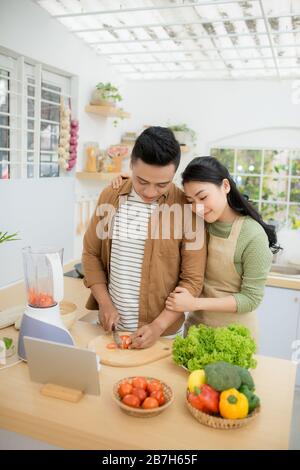Portrait of a pretty young couple cooking together according to a recipe on a tablet computer Stock Photo