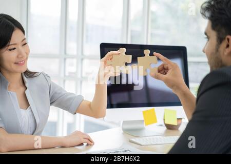 An asian business people sitting at office desk, putting puzzle pieces together, finding solution. Stock Photo