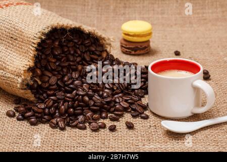 Cup of coffee, macaroons and roasted coffee beans in a canvas sack on sackcloth. Stock Photo
