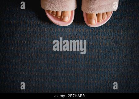 female legs with a pedicure in pink fluffy slippers on a dark blue carpet background. Copy space, flat lay, minimalism. Stock Photo