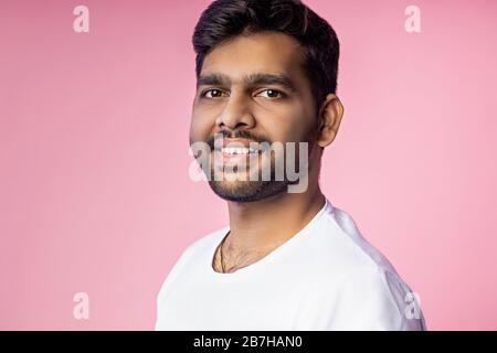 Horizontal close up portrait of handsome young indian man with stubble, wearing white t shirt, looking at camera with serious, calm expression, isolat Stock Photo