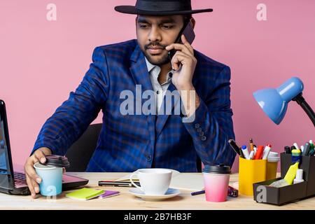 Shot of bearded stylish young businessman in formal wear, having phone conversation with partner, discussing terms of deal, drinking coffee, siiting a Stock Photo