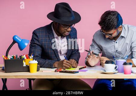Closeup cropped shot of african young entrepreneur and manager discussing joint project or terms of the deal, holding pens, sitting at desk in office. Stock Photo
