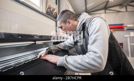 Electrical engineer operator repairs large premium industrial printer and plotter machine in digital printshop office Stock Photo