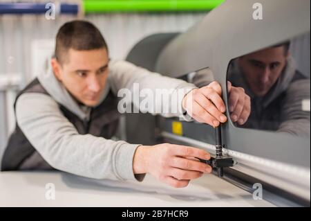 Electrical engineer operator repairs large premium industrial printer and plotter machine in digital printshop office Stock Photo