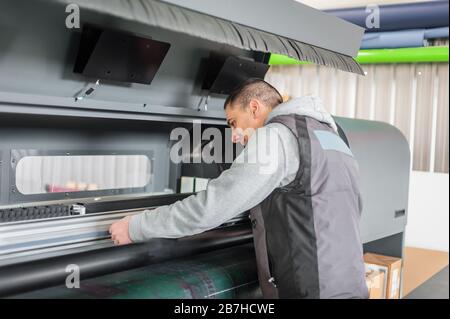 Electrical engineer operator repairs large premium industrial printer and plotter machine in digital printshop office Stock Photo