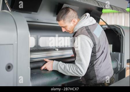 Electrical engineer operator repairs large premium industrial printer and plotter machine in digital printshop office Stock Photo