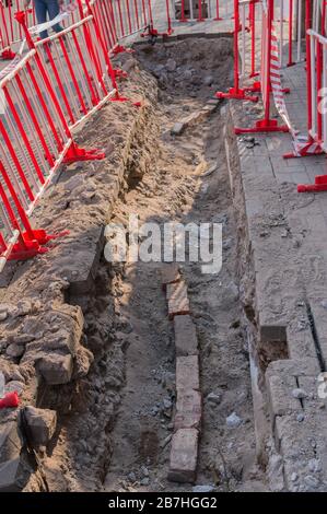 Danger for pedestrians on the street. A pit on the sidewalk, surrounded by red and white warning barriers. Repair of paving slabs. Stock Photo
