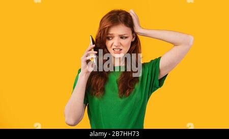 Confused Girl Talking On Phone Standing Over Yellow Background, Panorama Stock Photo