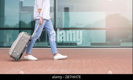 Travelling And Transportration. Male traveler walking with suitcase against airport building Stock Photo