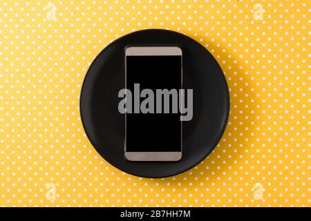 Smartphone on black plate and yellow background top view Stock Photo