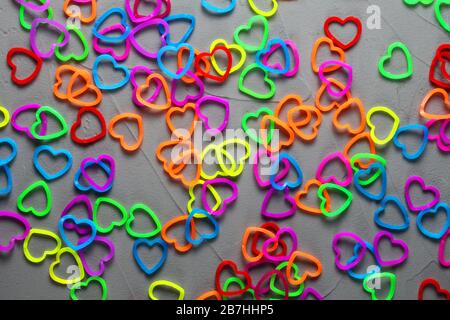 multi-colored elastic bands for weaving in the form of hearts are scattered on a concrete background Stock Photo