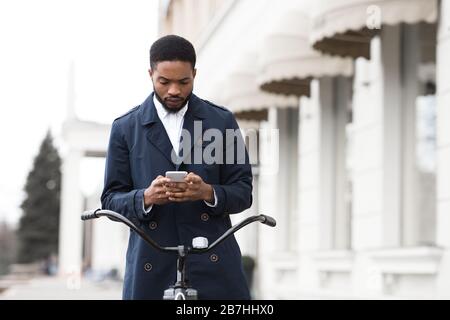 Handsome businessman texting on cellphone sitting on bicycle Stock Photo