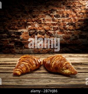 Fresh croissants on desk and free space for your decoration.Dark mood photo of wall with shadows.Copy space for your composition. Stock Photo
