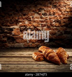 Fresh croissants on desk and free space for your decoration.Dark mood photo of wall with shadows.Copy space for your composition. Stock Photo