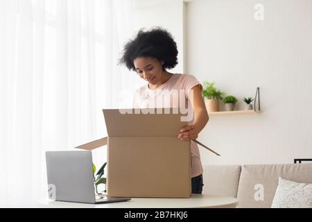 Surprised american young woman with laptop opens box Stock Photo