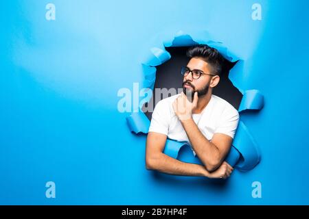 Young handsome indian man thinking look from blue paper hole Stock Photo