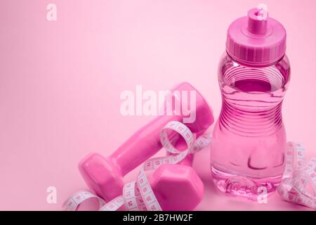 Dumbbels, measuring tape and bottle of water on pink background Stock Photo