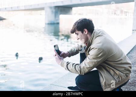 young male taking photos outdoors by mobile phone Stock Photo
