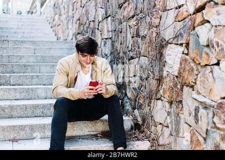 Young man using mobile phone while sitting outdoors Stock Photo