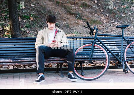 Young man using mobile phone while sitting outdoors Stock Photo