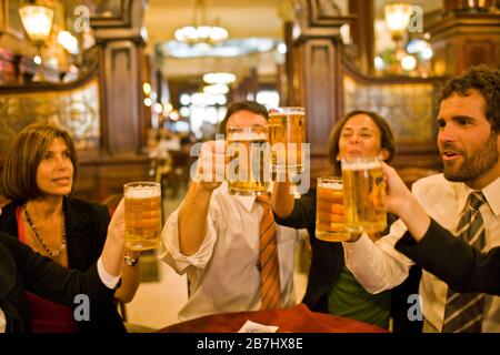 Happy business people raising beer glasses in a toast while sitting at a table in a restaurant. Stock Photo