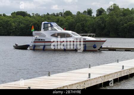 White motor cruiser moored alongside wooden jetty on Lower Lough Erne a popular location for a sailing holiday in Northern Ireland. Stock Photo