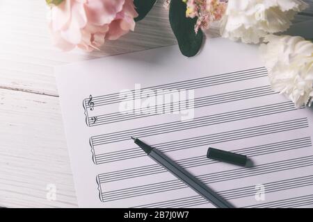 blank music notes sheet with flowers and pen on white wooden table Stock Photo