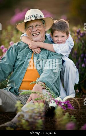 Boy hugging his grandfather as they sit outside. Stock Photo