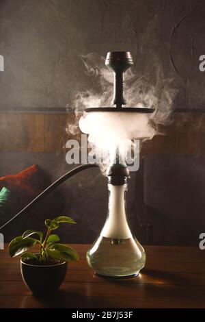 Smoke from a hookah in a bar on a table on a dark background. Smoking for relaxation. Stock Photo