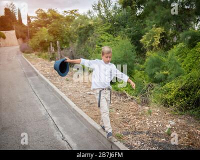 boy walks along the curb with a hat in his hands. Stock Photo