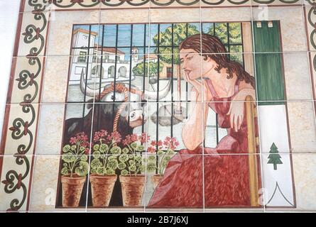 Spanish woman in a red dress, with a tame bull and flowers. Picture painted on tiles on a wall In Zahara de la Sierra, Cadiz,  Andalucia, Spain. Stock Photo