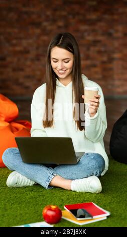 Girl in workspace working on laptop and drinking coffee Stock Photo
