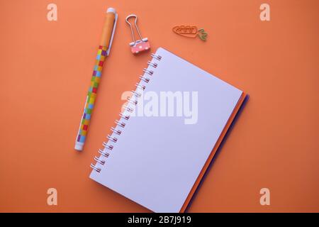 Wide view of blank spiral note pad and pen on orange color background  Stock Photo
