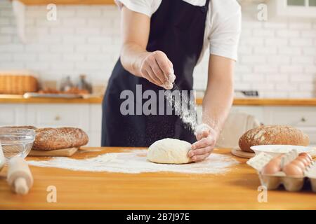 Baker male bearded man makes fresh bread dough at a table in the bakery kitchen. Stock Photo