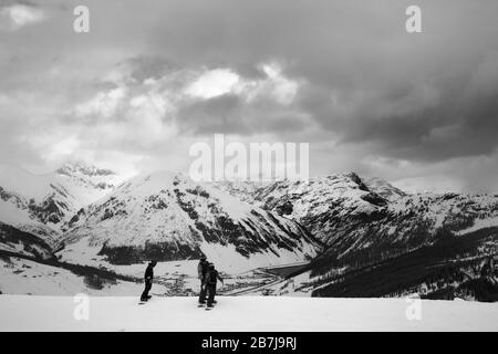 Group of snowboarders starts on off-piste descent. High snowy mountains and cloudy storm sky at winter before blizzard. Italian Alps. Livigno Lombardy Stock Photo