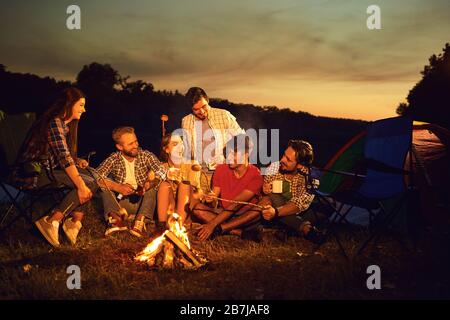 A group of people sitting by the bonfire next to the tent at night in the summer in autumn. Stock Photo