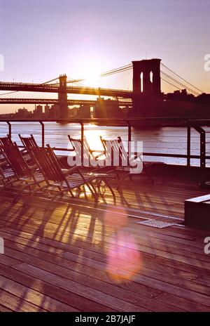 USA. New York. Brooklyn Bridge on East River sunrise view from boardwalk with deck chairs. Stock Photo