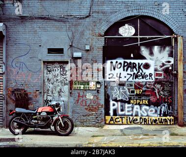 USA. New York. Moto Guzzi motorcycle standing by graffiti-covered building. Stock Photo