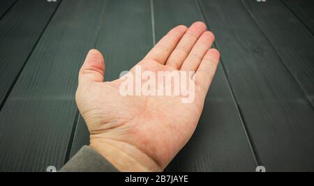 Front of a white adult man's hand outstretched on a gray wooden table Stock Photo