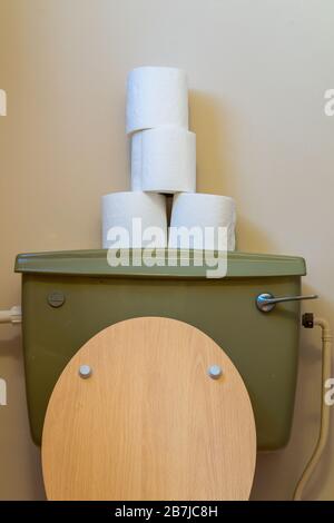 Stacked up toilet paper rolls on top of a water cistern in a UK bathroom Stock Photo