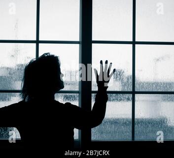 Woman looking out of window on rainy day. Conept image; female depression, domestic abuse, self isolation, quarantine, Coronavirus, Stock Photo