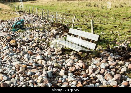 A wooden bench surrounded by rocks and boulders thrown up by hurricane Gonzalo near Dunrobin Castle at Golspie, Sutherland, Highlands, UK Stock Photo