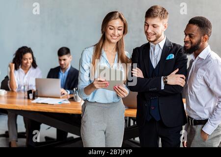 Coworkers Holding Digital Tablet Discussing Business News Standing In Office Stock Photo