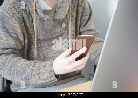 Man sitting at desk in front of computer using phone for 2 factor authentication concept conceptual 2FA 2 FA 2 factor two factor auth secure security Stock Photo
