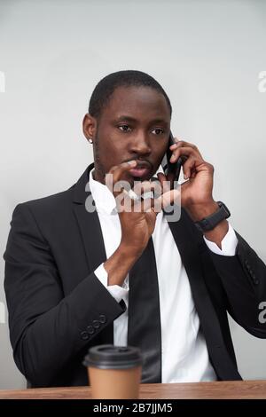 Closeup of angry young african man screaming while talking on smartphone over grey background Stock Photo