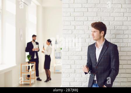 Serious businessman in casual attire standing in a white office on a white wall. Stock Photo